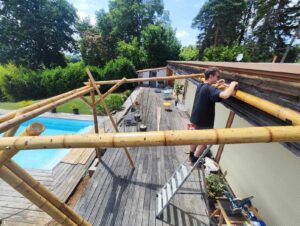 Assemblage des poteaux et traverses en bambou sur une terrasse en bois, dans le cadre d’une pergola sur mesure.