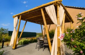 Pergola en bambou avec couverture naturelle et rideaux, aménagée sur une terrasse de jardin avec un espace repas.