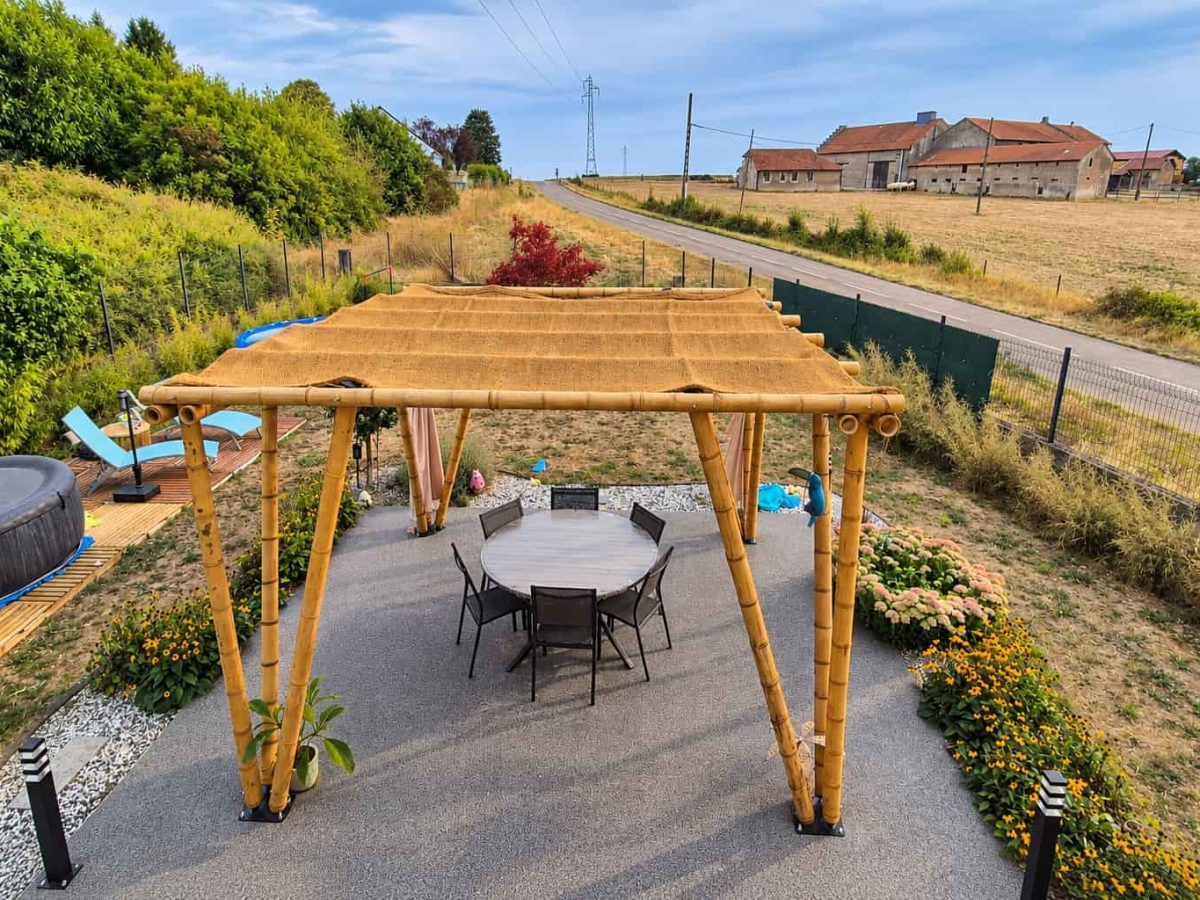 Vue en hauteur d'une pergola en bambou avec couverture d'ombrage naturelle, installée au-dessus d'un salon de jardin.