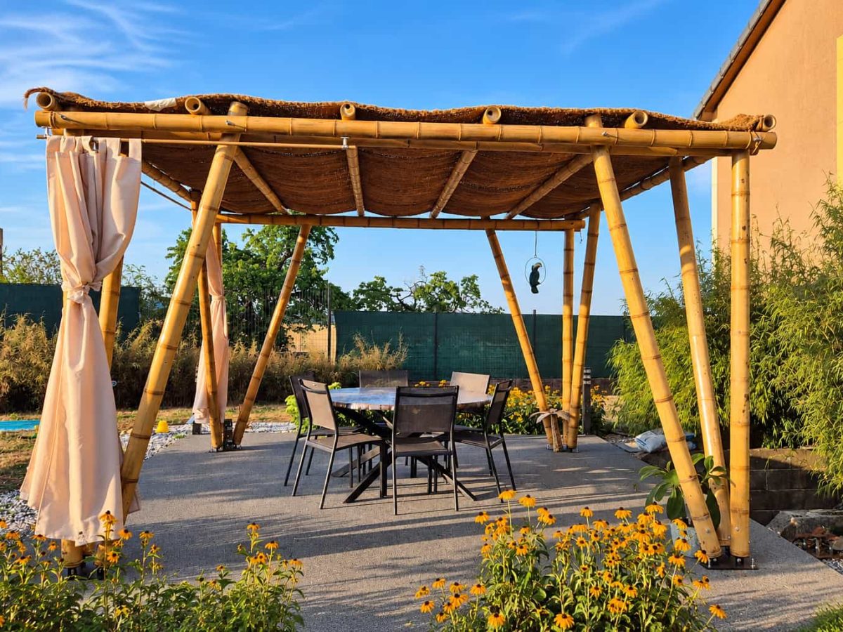 Pergola réunionnaise autoportée en bambou de 4 × 4 m avec toile de coco, jambes de force inclinées et espace repas aménagé sur une terrasse.