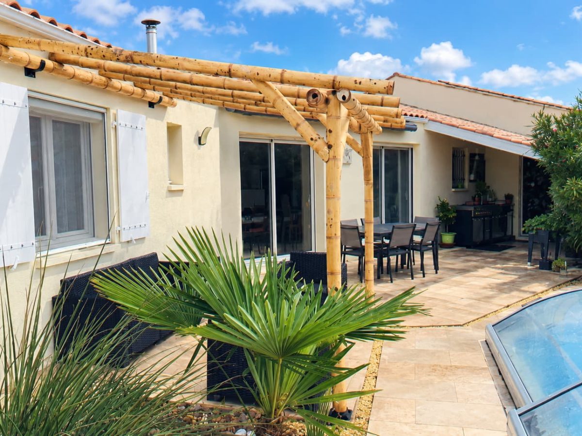 Pergola en bambou Guadua adossée à une maison, installée sur une terrasse à proximité d'une piscine.